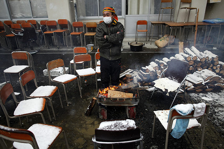 japan disatster: A survivor warms himself by a fire at an emergency shelter in Otsuchi