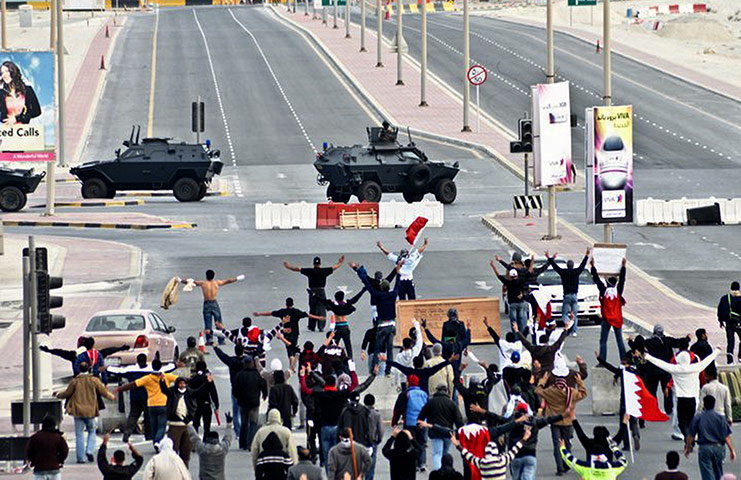 Bahrain uprising: Anti-government protesters wave in front of military vehicles