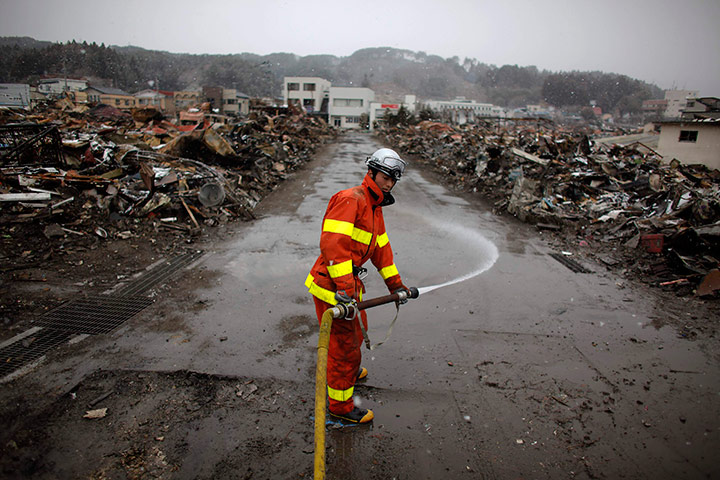 Japan aftermath: A fireflighter sprays water to clean a street in the debris in Yamada