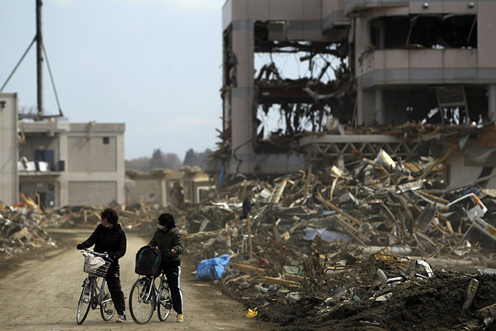 Japan Earthquake: Two girls ride their bicycles near debris, Rikuzentakata, Iwate prefecture