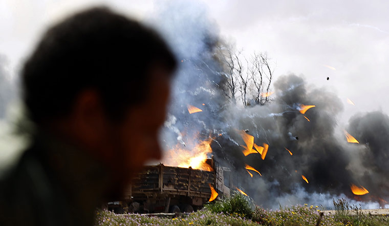 Libya airstrikes: A rebel fighter looks at burning vehicles after an air strike 