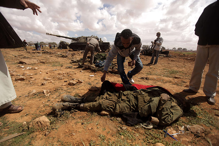 Libya airstrikes: A Libyan rebel empties the pockets of a member of Muammar Gaddafi's forces