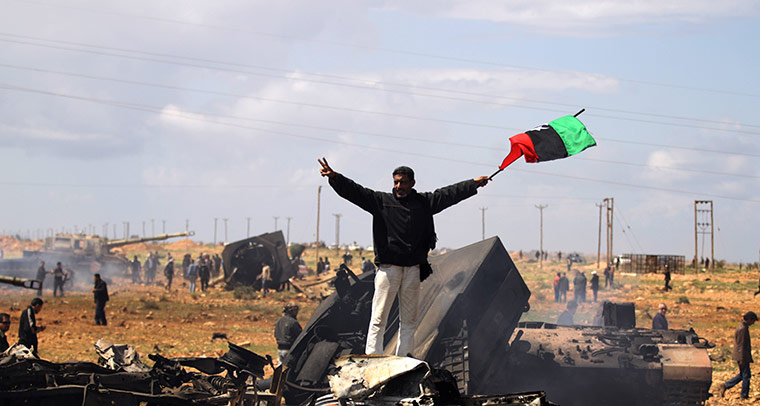 Libya airstrikes: A Libyan rebel waves a flag as he stands on wrecked military vehicles 