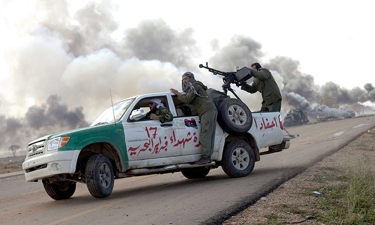 Libya airstrikes: Libyan rebel soldiers drive by burning vehicles hit by coalition forces 