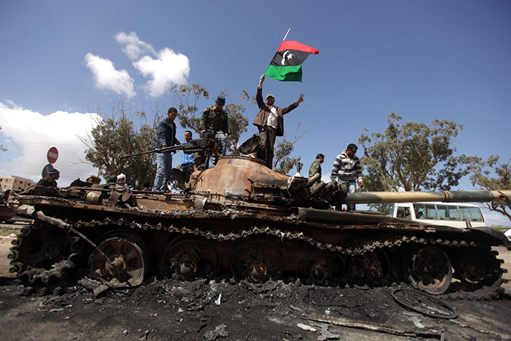 Libya airstrikes: Libyan rebels wave their flag on top of a wrecked tank near Benghazi 