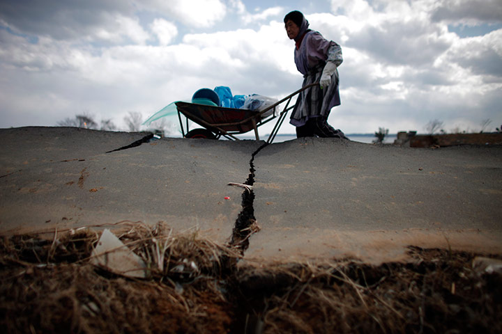 Japan survivors: A woman pushes a wheelbarrow as she clears her house, Japan