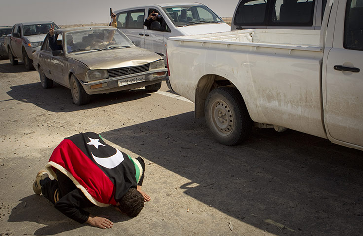 Ajdabiya seized by rebels: A rebel, draped in the old Libyan flag, prays at the entrance to the city