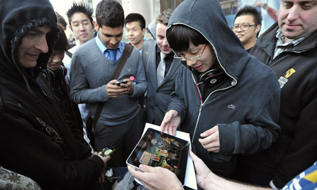 Shoppers look at an iPad as they queue o