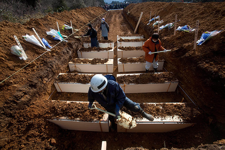 Japan aftermath: Japanese workers shovel dirt on to coffins during a mass funeral,
