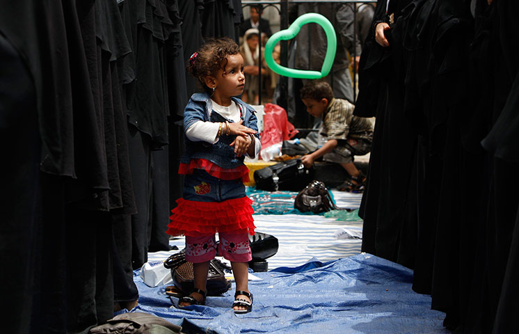 24 hours in pictures: A girl stands beside women praying during an anti-government rally, Yemen