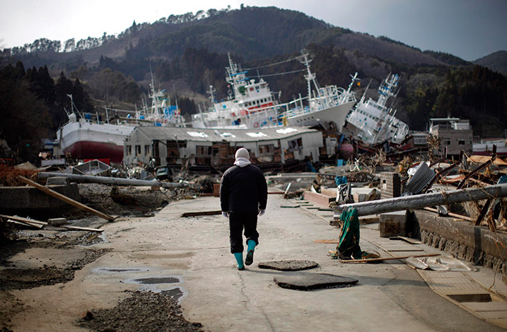 Japan: A man walks next to a destroyed port area in Kessenuma
