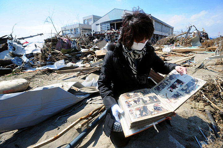 Japan: A woman looks through a family album found by destroyed house, Sendai