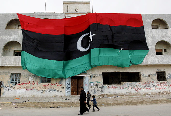 libya unrest continues: Libyan citizens pass a building dressed with a huge old Libyan flag