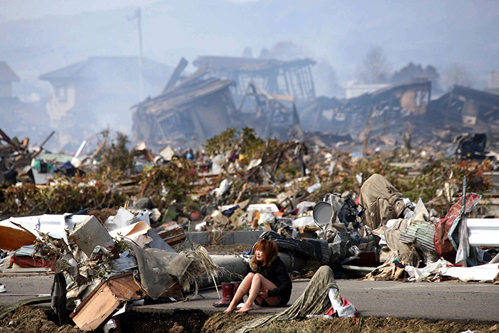 Japan disaster 1 month on: A woman cries while sitting on a road amid rubble in Natori