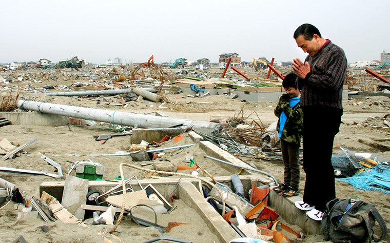 Japan disaster 1 month on:  A man and his grandson offer a prayer at the ruins of a house in Natori 