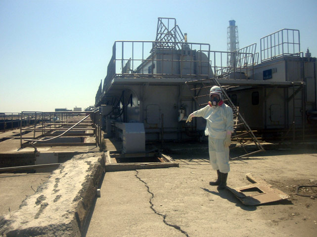 Fukushima disaster: 2 April:A worker wearing a protective suit points at a cracked concrete pit