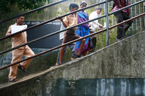 A child is helped up the steps to his school by his mother in India.