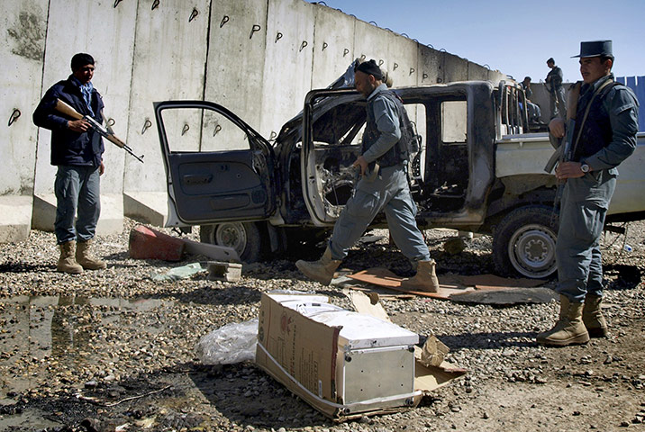 Afghanistan protests: An Afghan policeman walks past by a burnt vehicle at the UN compound