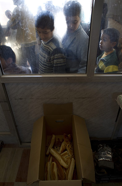 Life in masrata libya: Two young boys looks through a window at a few loafs of bread 