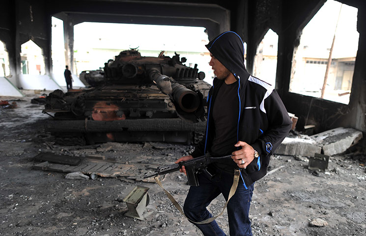 misrata: A rebel walks past a pro-Gaddafi tank that was destroyed by a NATO bombing
