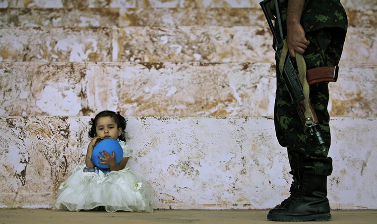 24 Hours: A girl holding a balloon sits on the ground next to a guard in Yemen