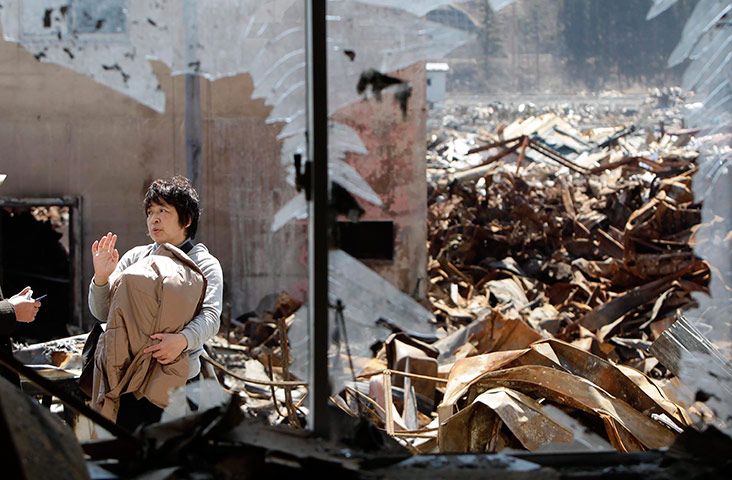 24 hours in pictures: Tsunami survivor carries an urn in front of the ruins of her house, Japan