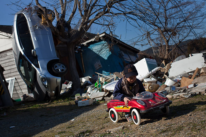 24 hours in pictures: A boy plays in a toy car in front of a washed up car, Japan