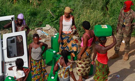 A soldier loyal to Alassane Ouattara, right, looks on as women venture out in search of water