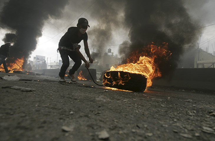 Israel violence: A Palestinian protester stands next to a burning barricade