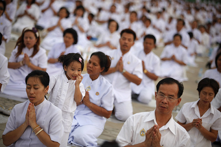 24 hours in pictures: A girl plays behind her mother as Buddhists believers pray, Bangkok