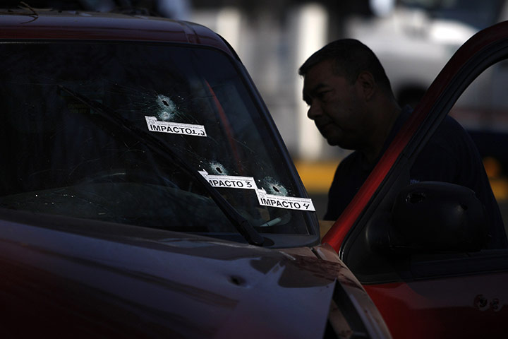 24 hours: Guadalajara, Mexico: A police officer stands next to a bullet-riddled car