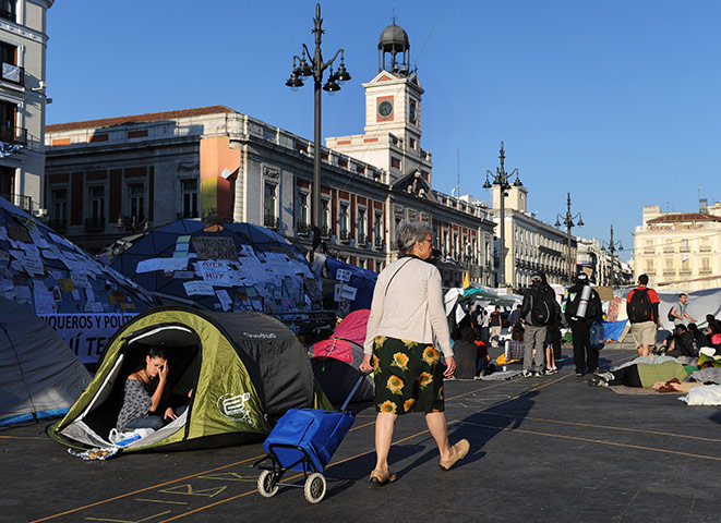 Spain protests continue: A woman passes tents and banners of protestors continuing to camp out