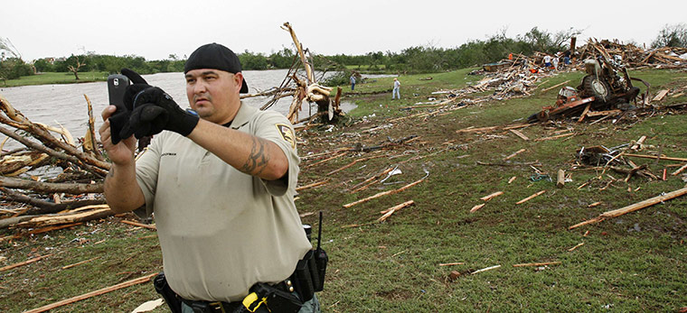 Tornadoes in US: A Sheriff Deputy akes a photo of the debris path of a tornado