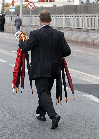 G8 summit: A man holds umbrellas as he follows the G8 leaders while they walk in rain