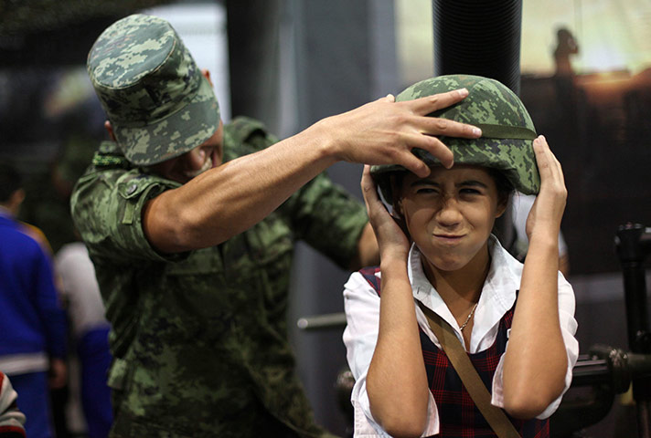 24 hours in pictures: A soldier helps a girl to adjust a helmet during an army exhibition, Mexico