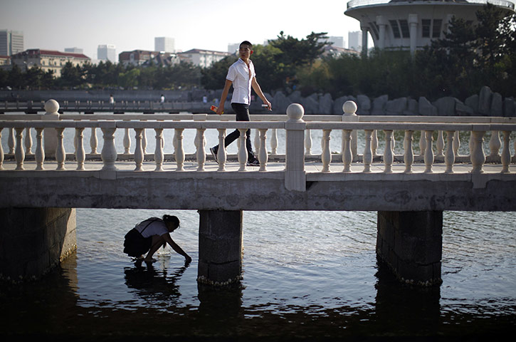 24 hours: Weihai, China: A woman looks for crabs under a bridge 