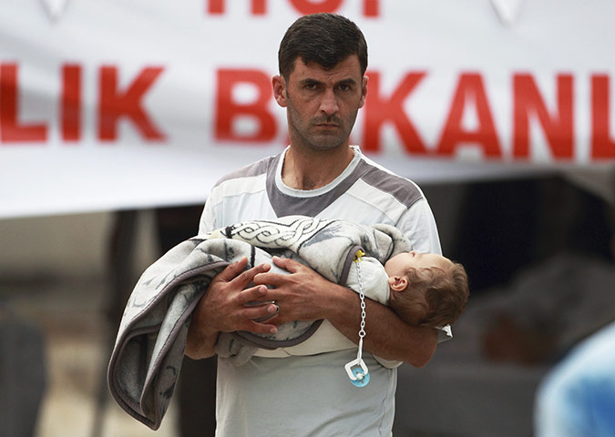 syrian refugees: Man carrying a baby enters a medical tent at refugee camp in Yayladagi