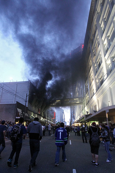 Vancouver riots: People walk in the street as smoke billows out of a building in Vancouver