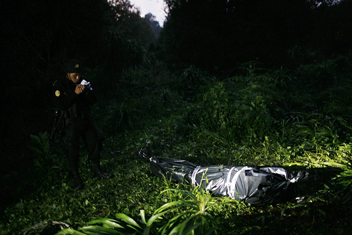 Guatemala gang wars: A police officer stands guard next to a covered body