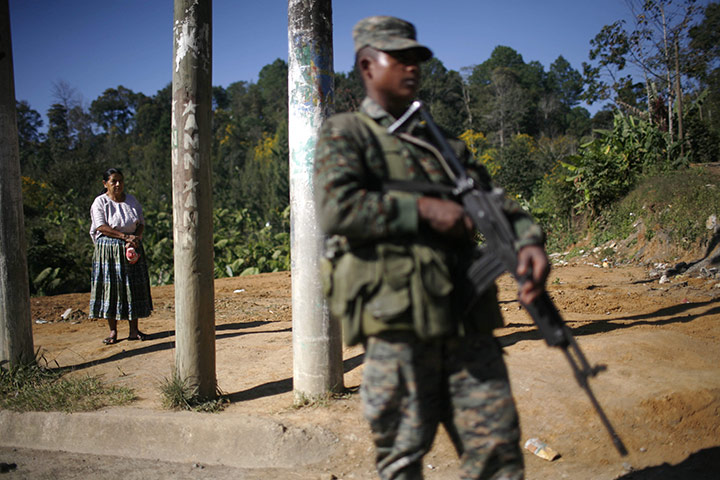 Guatemala gang wars: A woman waits for a bus as a soldier stands guard