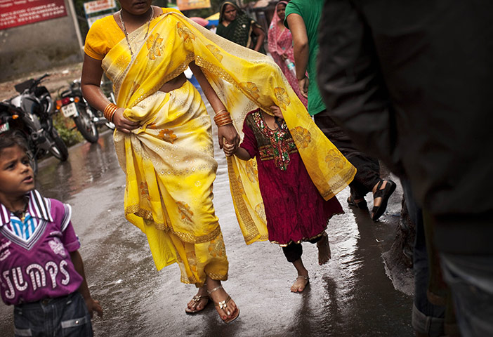 24 hours in pictures: A girl covers herself with her mother's sari during heavy rains in India