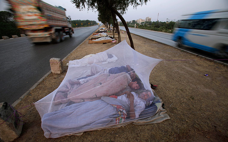 24 hours in pics: Vehicles move past Pakistan daily workers, sleeping under a mosquito net