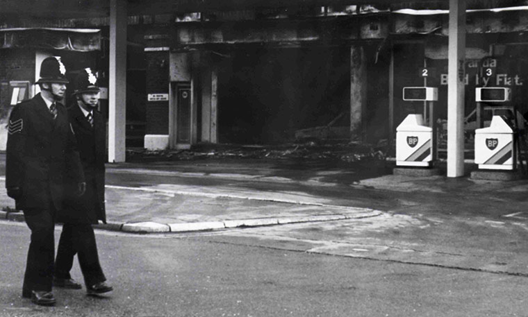 Toxteth Riots: Two policemen walk past a burnt out BP garage