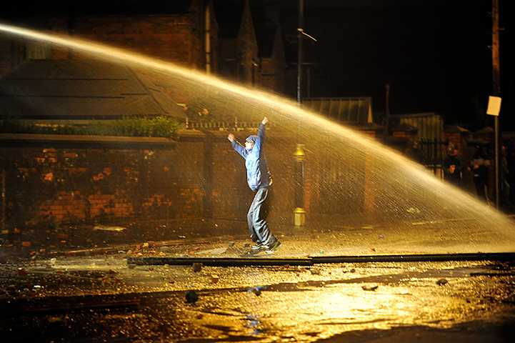 Ardoyne riots: A Nationalist youth dances in defiance as police fire a water cannon