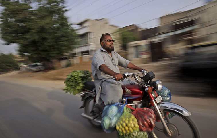 24 hours in pictures: A man rides his motorcycle loaded with bags full of vegetables in Pakistan