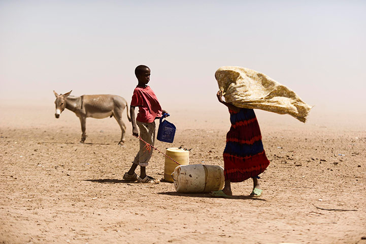 24 hours in pictures: People and a donkey stand near water containers in Wajir