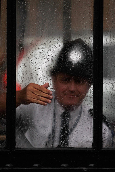 24 hours in pictures: A Police officer shelters from torrential rain, London