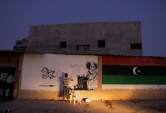 24 hours in pictures: A street artist paints a caricature of Libyan dictator Muammar Gaddafi