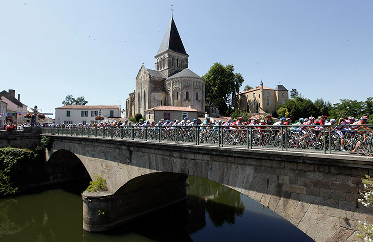 Tour de France stage 1: The peloton streams over a bridge as they pass a church at Mareuil-sur-Lay 
