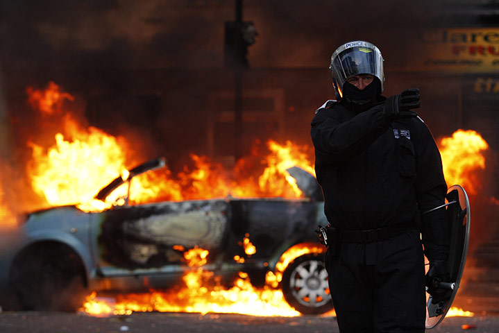 Seven days on stage: Riot police officer directs people away from a burning car in Hackney
